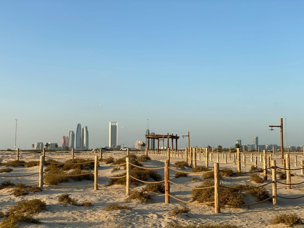 Sunny desert landscape with Abu Dhabi skyline in the background, showcasing modern architecture and clear blue skies.